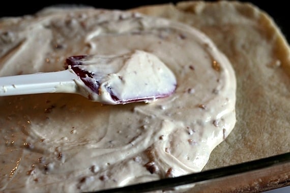 Toffee cheesecake batter being spread over crust in a baking dish