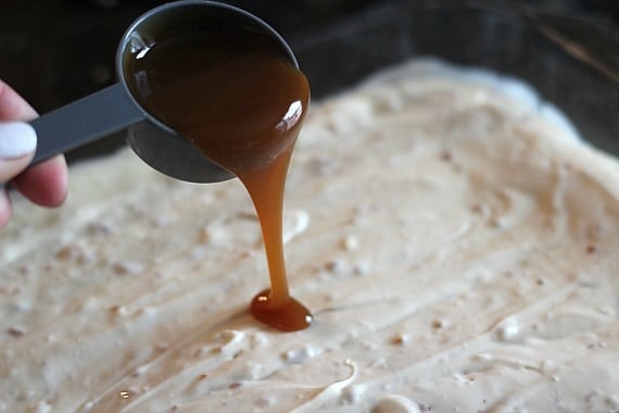 Caramel sauce being poured over toffee cheesecake batter in a baking dish