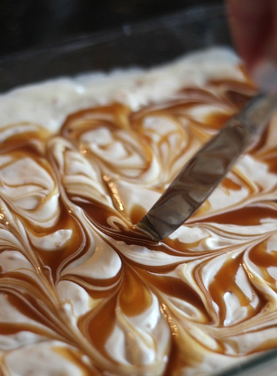 Caramel sauce being swirled into cheesecake batter in a baking dish