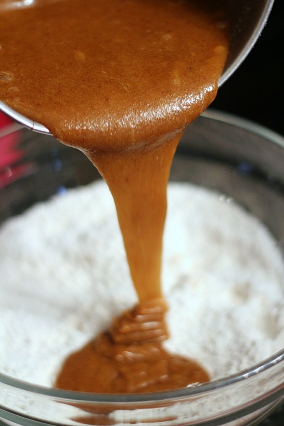 Melted brown sugar mixture being poured into a mixing bowl of dry ingredients.