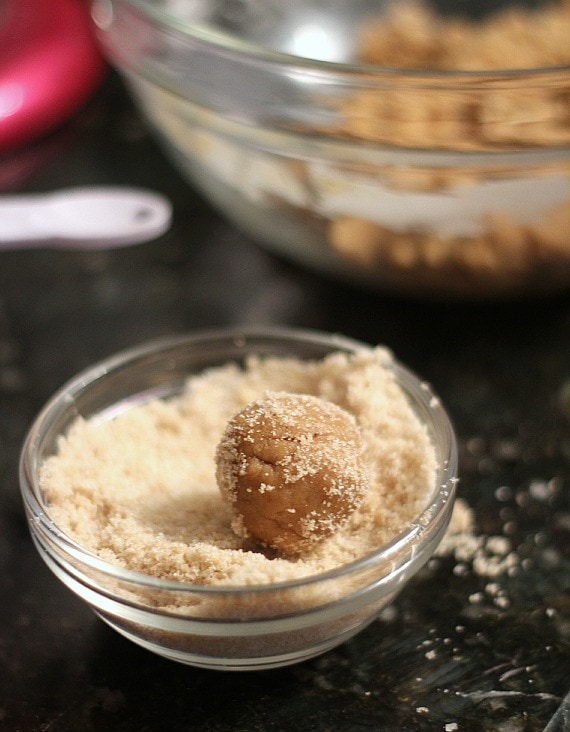 Brown sugar cookie dough ball being rolled in a bowl of brown sugar