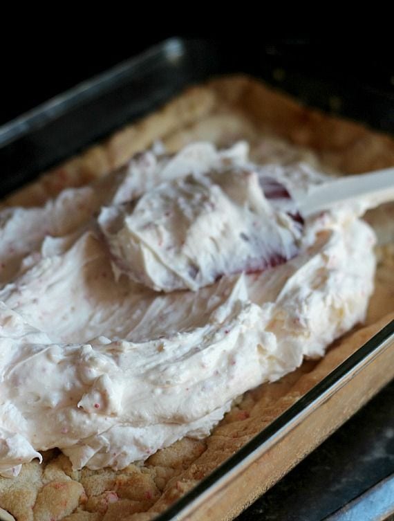 Peppermint cream cheese frosting being spread over peppermint cookie bars in a 9x13 baking dish