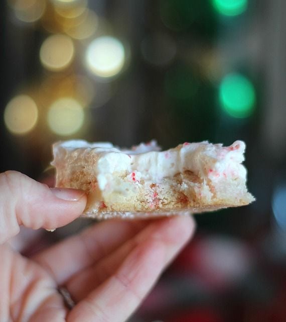 A hand holding a square of peppermint cookie bars with peppermint cream cheese frosting