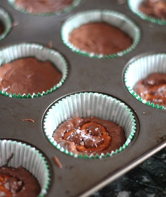 Crockpot candy inside a lined muffin pan, topped with pretzels.