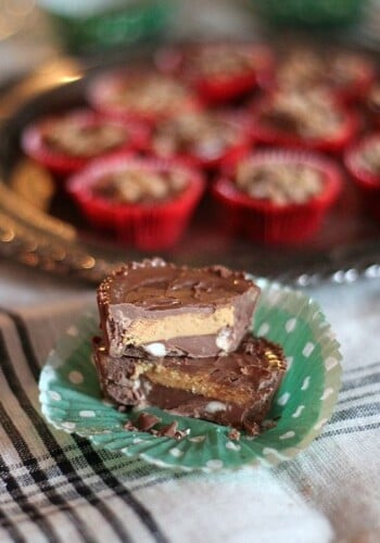 Two crock pot candies stacked inside an unfolded cupcake liner, with a tray of chocolate candies in the background.