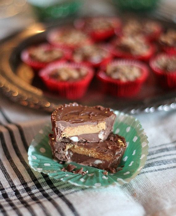 Two crock pot candies stacked inside an unfolded cupcake liner, with a tray of chocolate candies in the background.