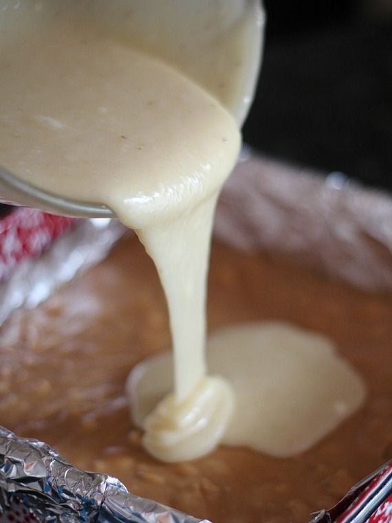 Banana fudge batter being poured over peanut butter fudge layer in a foil-lined pan