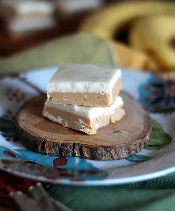 Two squares of Peanut Butter Banana Fudge stacked on a piece of wood on a plate
