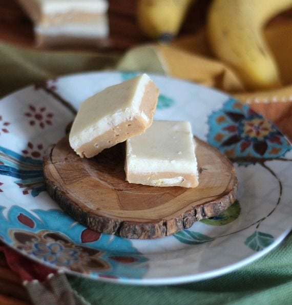 Two squares of peanut butter banana fudge on a piece of wood on a plate