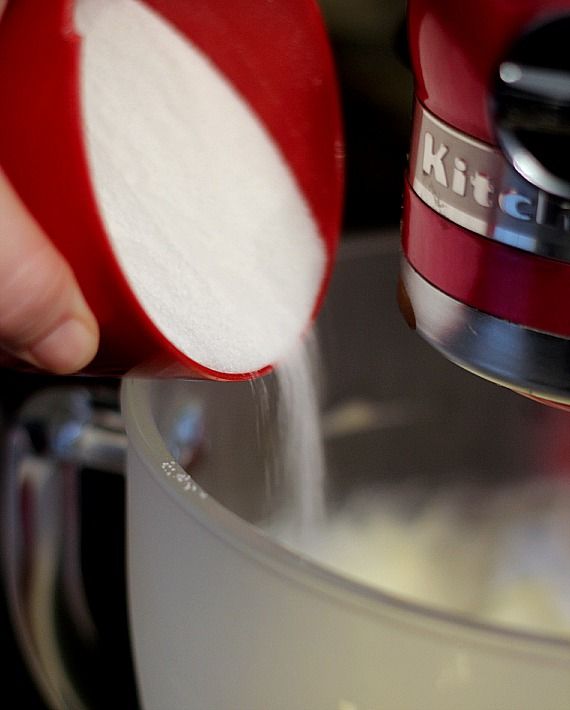 A scoop of white sugar being added to a stand mixer bowl