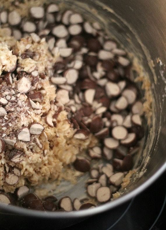 Chopped malted milk balls and rice krispies in a mixing bowl with melted marshmallow mixture