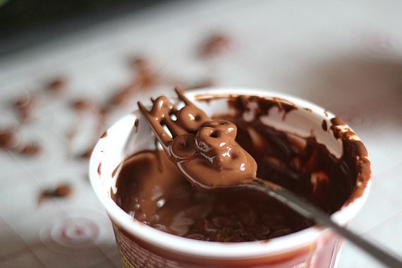 Chocolate covered cheerios on a fork over a cup of melted chocolate