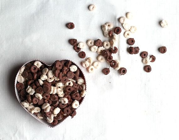 Dark and white chocolate covered cheerios in a heart-shaped tin and spread around outside the tin