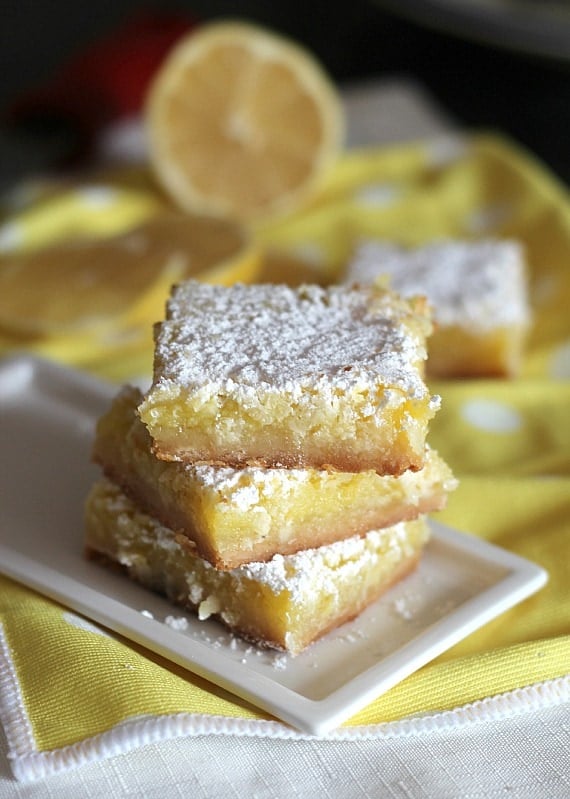 A stack of three coconut lemon squares are held on a small rectangular plate.