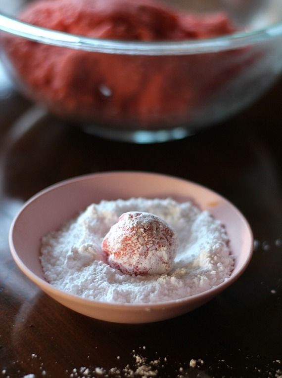 A strawberry cake mix cookie dough ball is rolled in a bowl full of powdered sugar.