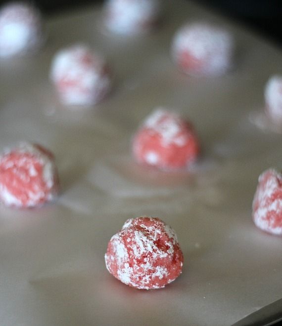 Balls of strawberry cake mix cookie dough on a parchment lined baking sheet.