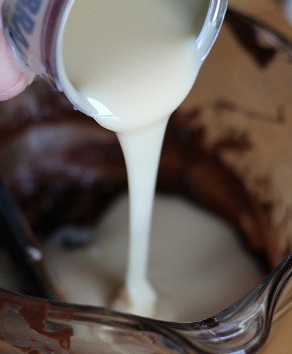 Sweetened condensed milk being poured into a bowl of melted chocolate