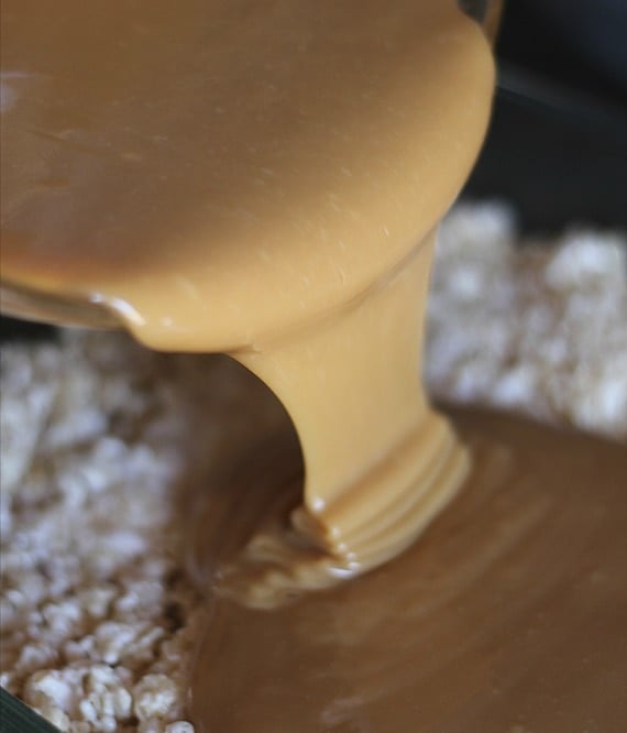 Caramel sauce being poured over rice krispie treats in a pan