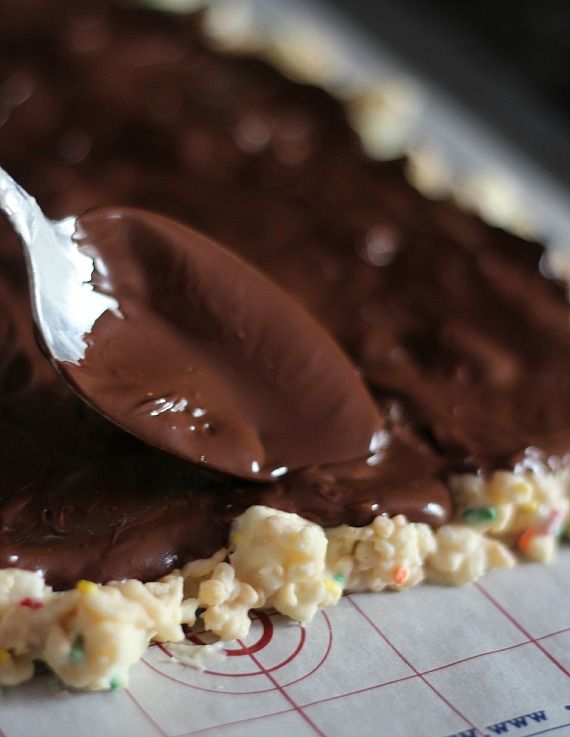 Melted chocolate being spread over rice krispie mixture on a baking sheet