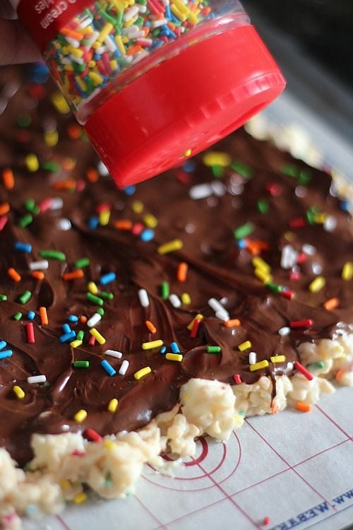 Rainbow sprinkles being added to chocolate-covered rice krispie treats