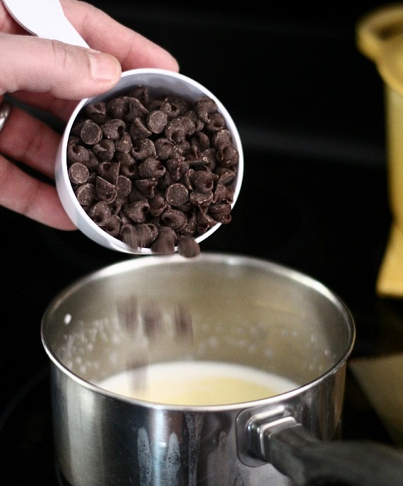 A scoop of chocolate chips being poured into a saucepan