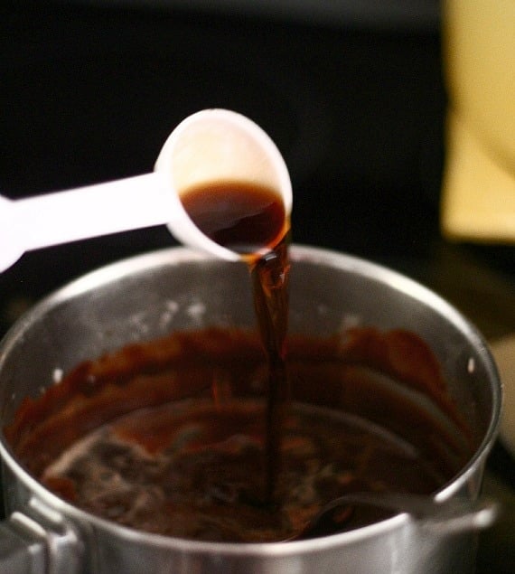A tablespoon of stout beer being poured into a saucepan of melted chocolate