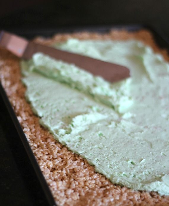 Green frosting being spread over rice krispie treats in a jelly roll pan