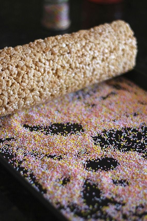 A rolled-up log of rice krispie treats with sprinkles spread on the work surface