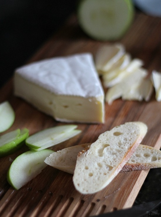 Thin slices of bread, Brie, and Granny Smith apple on a cutting board