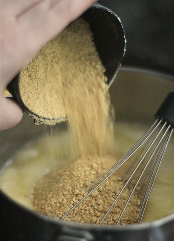 Graham cracker crumbs being poured into a bowl of batter with a whisk