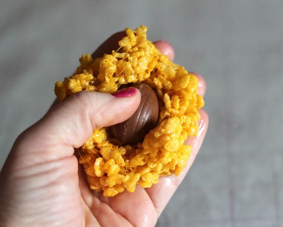 Mini cadbury egg being pressed into a circle of yellow rice krispie treat mixture