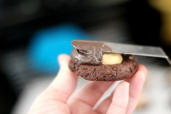 Chocolate frosting being spread over a peanut butter-filled chocolate cookie