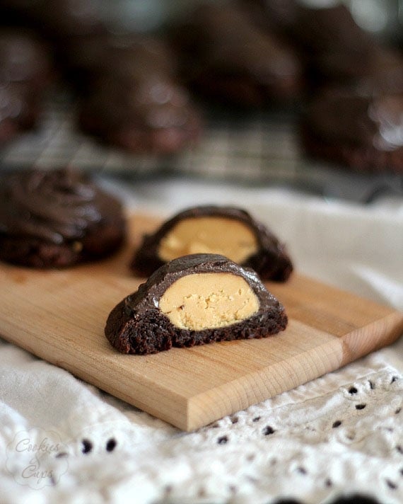 Buckeye Brownie Cookies on a wooden patter, with one cut in half to reveal the peanut butter center.