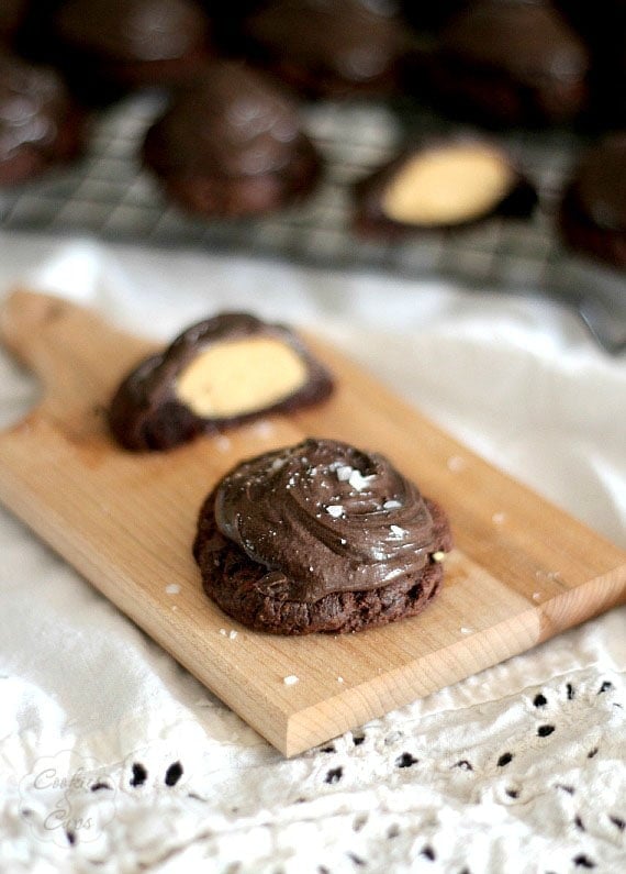 Two Buckeye Brownie Cookies on a wooden patter, with one cut in half to reveal the peanut butter center.