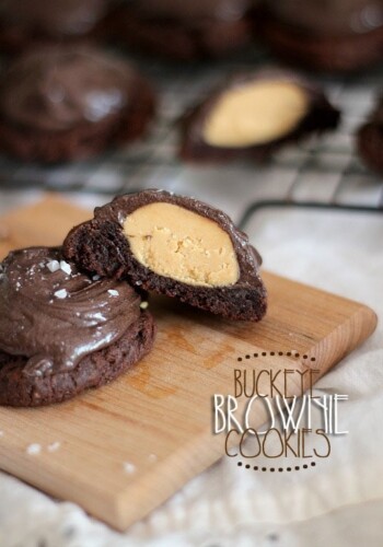 Two Buckeye Brownie Cookies on a wooden patter, with one cut in half to reveal the peanut butter center.