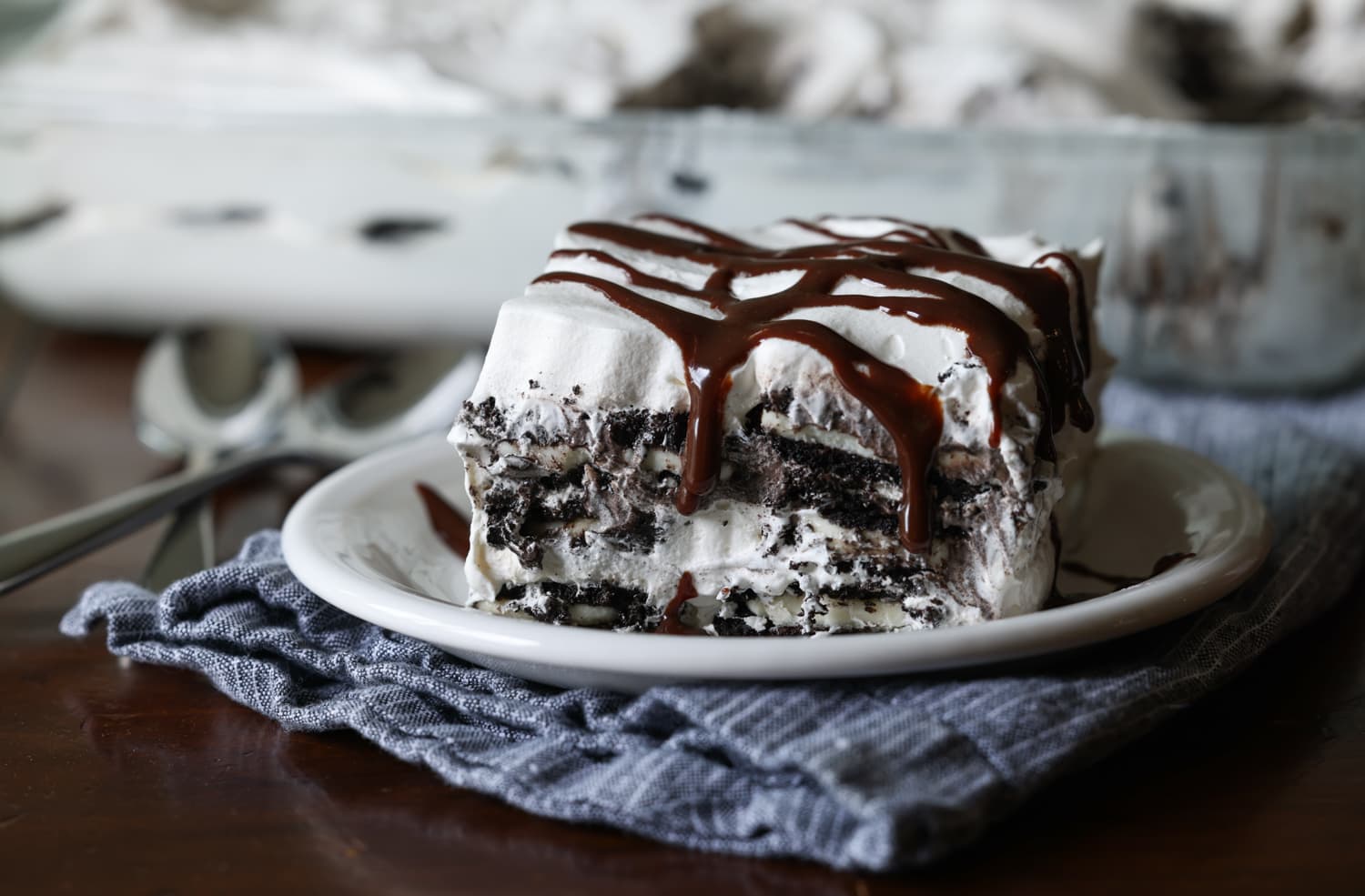 a piece of no bake icebox cake on a white plate with hot fudge on top and dripping down the sides.