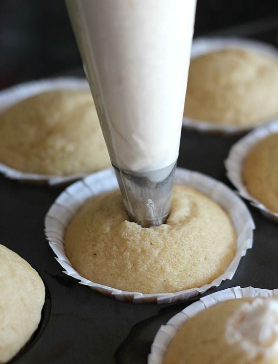 Cream filling being piped into the center of a vanilla muffin