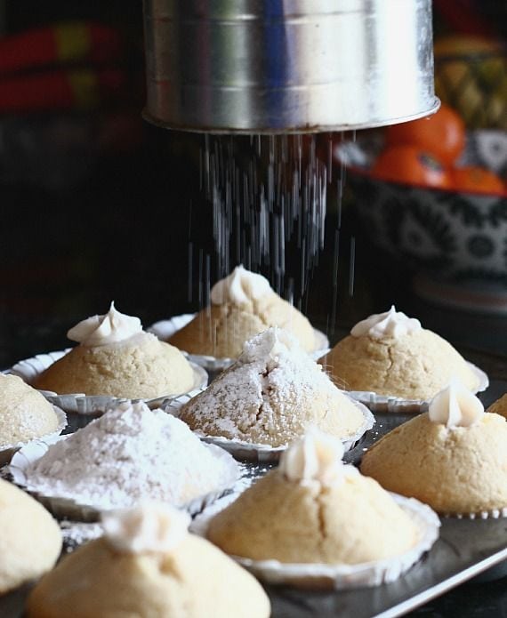Powdered sugar being sifted over cream-filled vanilla muffins in a muffin tin