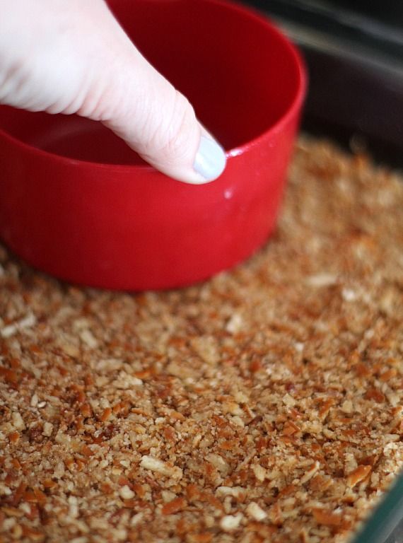 Pretzel crust being pressed into a pan with a measuring cup