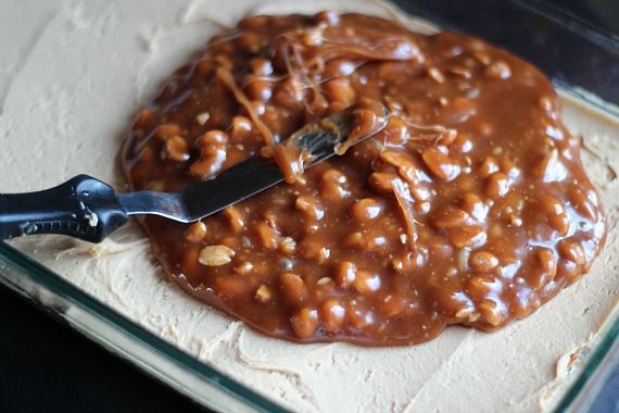 Peanut caramel sauce being spread over peanut butter filling and pretzel crust in a baking pan