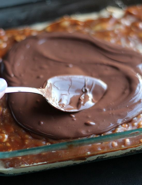 Melted chocolate being spread over caramel peanut mixture in a pan