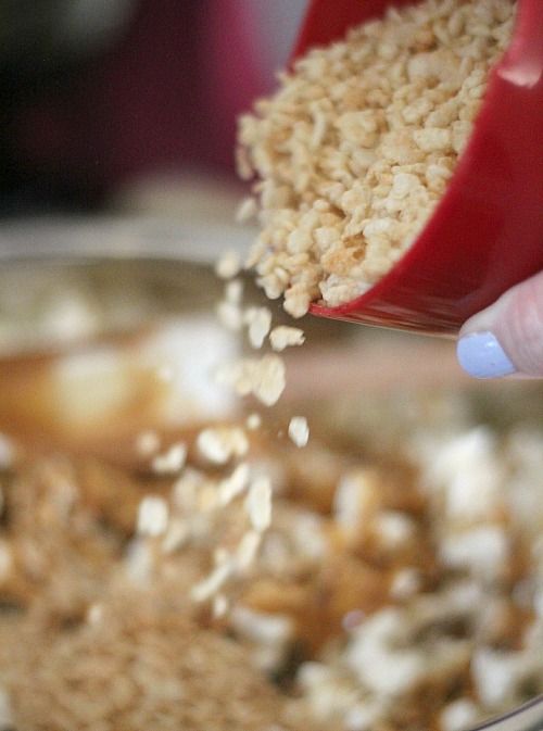 Rice krispie cereal being added to a bowl of popcorn with peanut butter caramel sauce