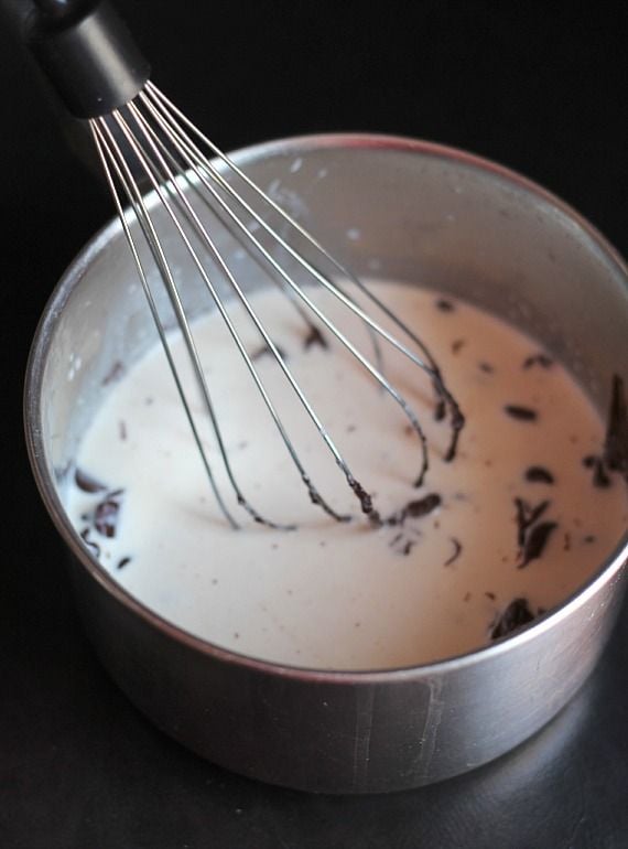 Overhead view of heavy cream and chocolate chips in a saucepan with a whisk