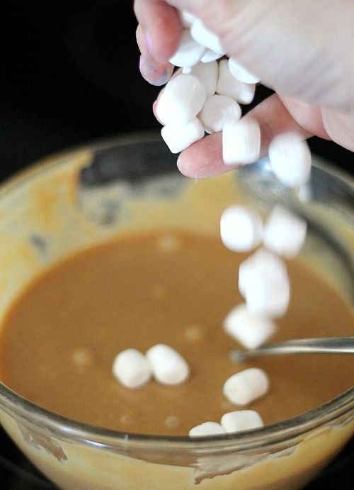 Mini marshmallows being added to a bowl of melted butterscotch mixture