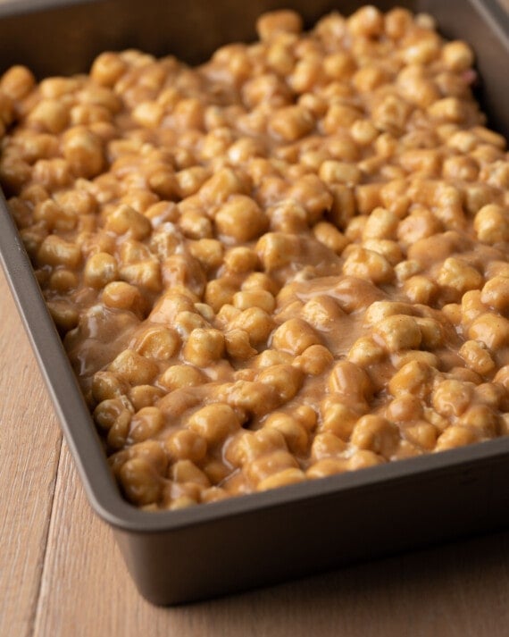 The marshmallow peanut butter layer is added overtop the peanuts in a baking pan.