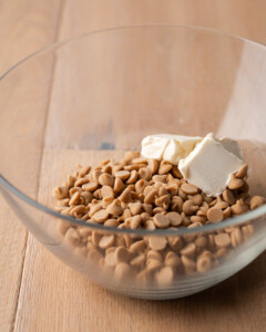 Peanut butter chips and butter in a clear mixing bowl.