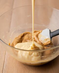 Sweetened condensed milk is drizzled into a mixing bowl with melted peanut butter chips and butter.