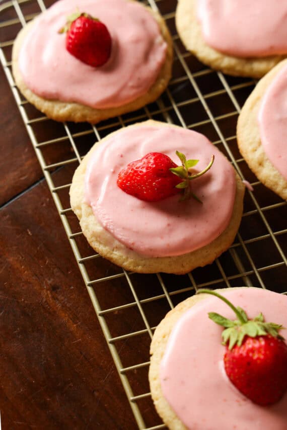 Strawberry cookies on a wire cooling rack topped with strawberry icing and a fresh strawberry