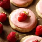 Strawberry Shortcake cookie topped with a fresh strawberry on a wooden plate surrounded by strawberries.
