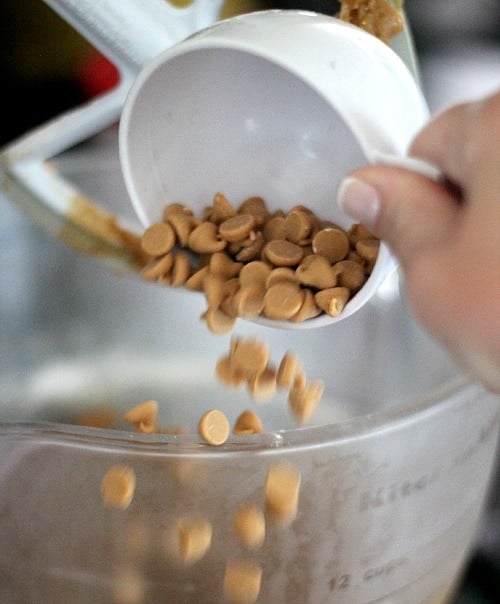 A cup of peanut butter chips being added to a mixing bowl